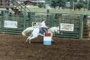 Girl riding white horse around a barrel